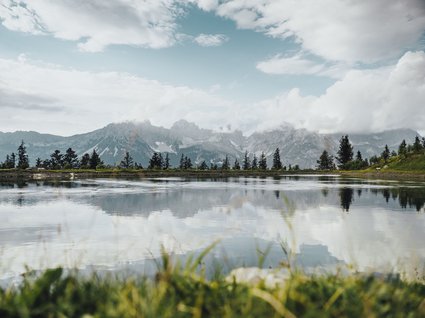 Discover the benefits of the Wilder Kaiser GästeCard to be used in your holiday area- Mountain lake with reflective water surface and cloudy sky