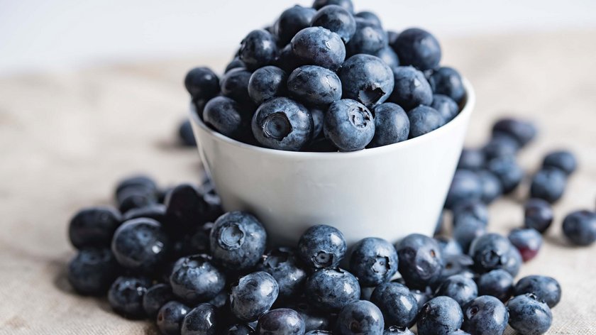 BLUEBERRIES – THE LITTLE MIRACLE BERRY Fresh blueberries in a white bowl and scattered on a cloth