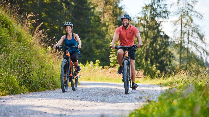 Mountainbiken am Wilden Kaiser: Adrenalin pur Frau und Mann fahren auf Waldweg Mountainbike, beide tragen Helme und Sportkleidung