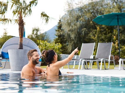 Holidays at the Postwirt: more than just in “a” hotel in Soll. Couple relaxing in pool with woman pointing and laughing outdoors
