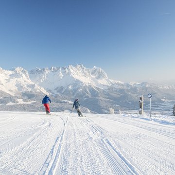 Holiday in Soll with children or as a couple Two skiers on snowy slope with Alps in background under clear blue sky