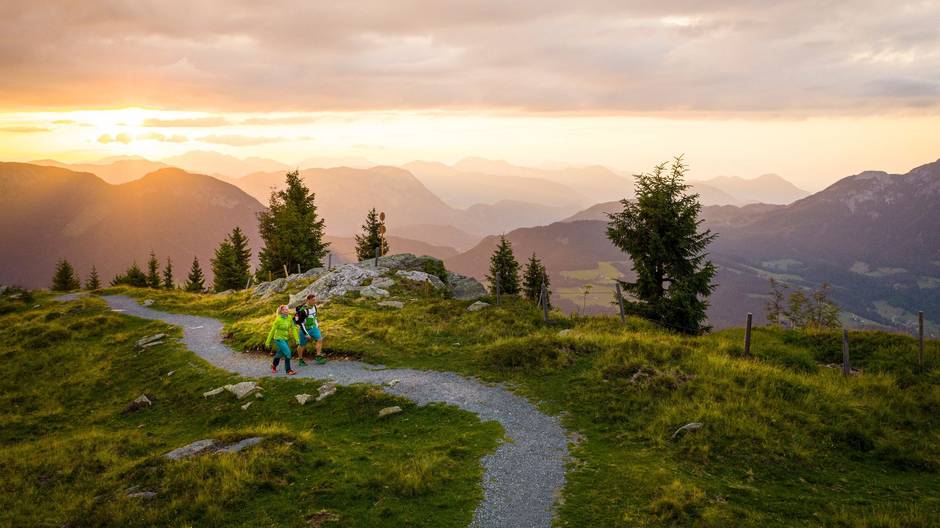 Discover the benefits of the Wilder Kaiser GästeCard to be used in your holiday area- Two hikers walking on a trail at sunset in the mountains