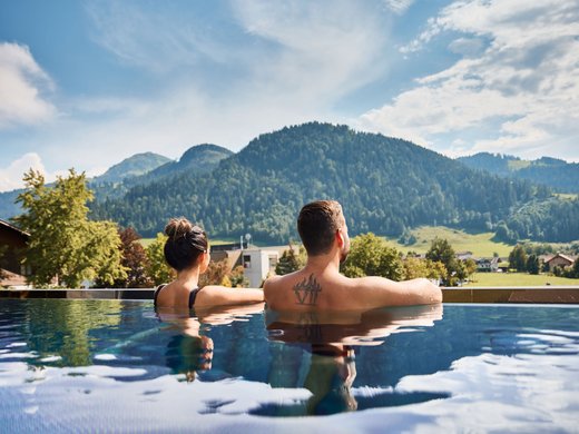Sie suchen ein Wellnesshotel in Tirol für adults only? Paar entspannt im Pool mit Bergblick unter blauem Himmel