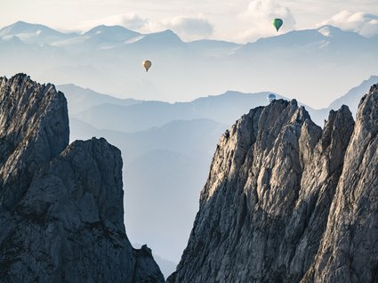 Discover the benefits of the Wilder Kaiser GästeCard to be used in your holiday area- Hot air balloons floating above rocky mountains with misty mountain layers in the background