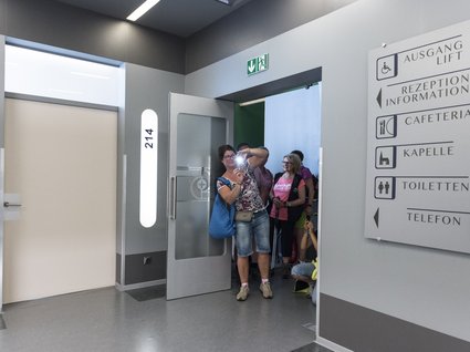 Die Drehorte von “Der Bergdoktor“ am Wilden Kaiser Gruppe Personen in einem Flur vor einem offenen Tür mit Wegweiser an der Wand