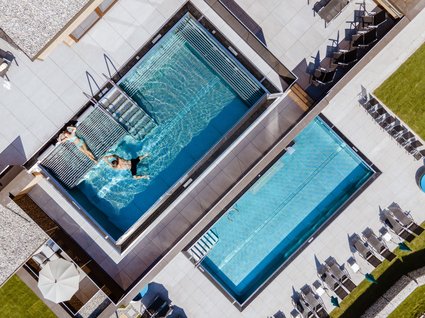 Der Postwirt: Hotel mit Infinitypool in Tirol Drohnenaufnahme von zwei rechteckigen Schwimmbecken mit Personen und Liegestühlen