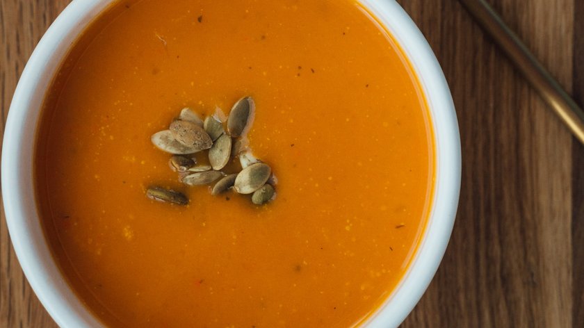 Herbstliche Verführung Kürbissuppe mit Kürbiskernen in einer weißen Schüssel auf Holztisch