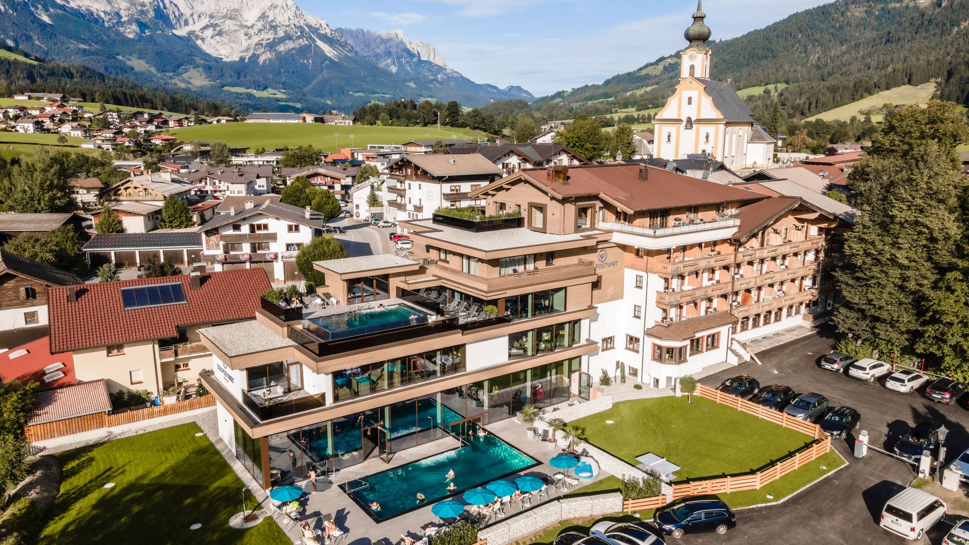 Hotel in Söll am Wilden Kaiser: der Postwirt Hotel mit Außen- und Dachpool im Tiroler Dorf vor Alpenbergen
