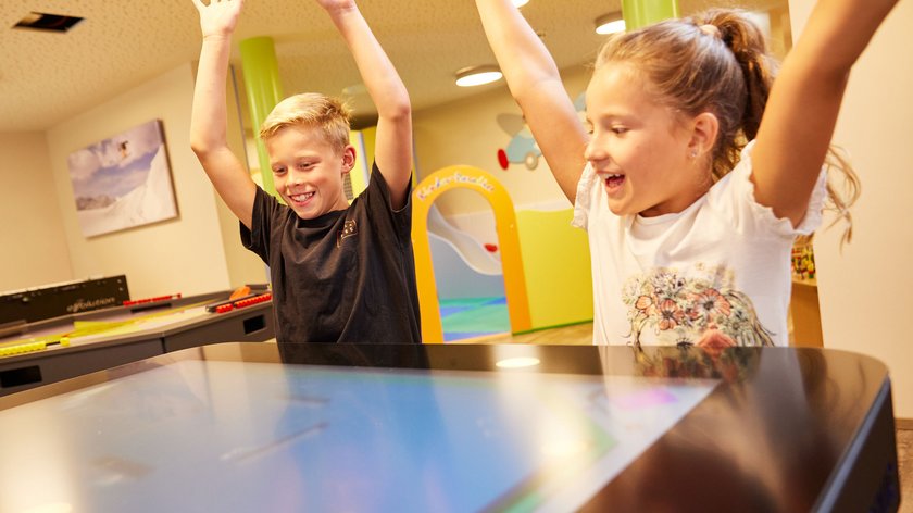Ein Urlaub voller Lachen und Abenteuer Zwei Kinder spielen an einem interaktiven Touchscreen mit erhobenen Armen