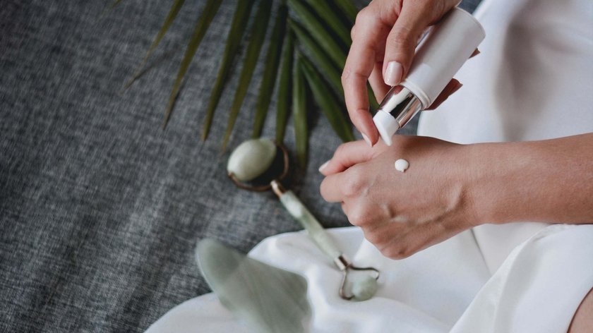 Kosmetik am Wilden Kaiser Hände tragen Creme auf, mit Jade-Gesichtsroller und Pflanzenblatt im Hintergrund