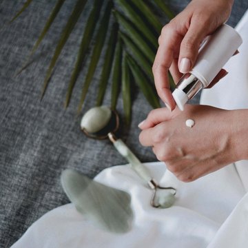 Urlaub in Söll mit Kindern oder als Pärchen Hände tragen Creme auf, mit Jade-Gesichtsroller und Pflanzenblatt im Hintergrund