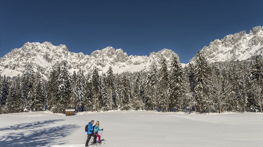 Die Schattseit-Winterrunde Zwei Skifahrer in blauer Winterkleidung im verschneiten Gebirge vor Tannenwald