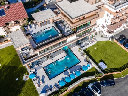 Holidays at the Postwirt: more than just in “a” hotel in Soll. Aerial view of a hotel with two outdoor pools and sun loungers with blue umbrellas