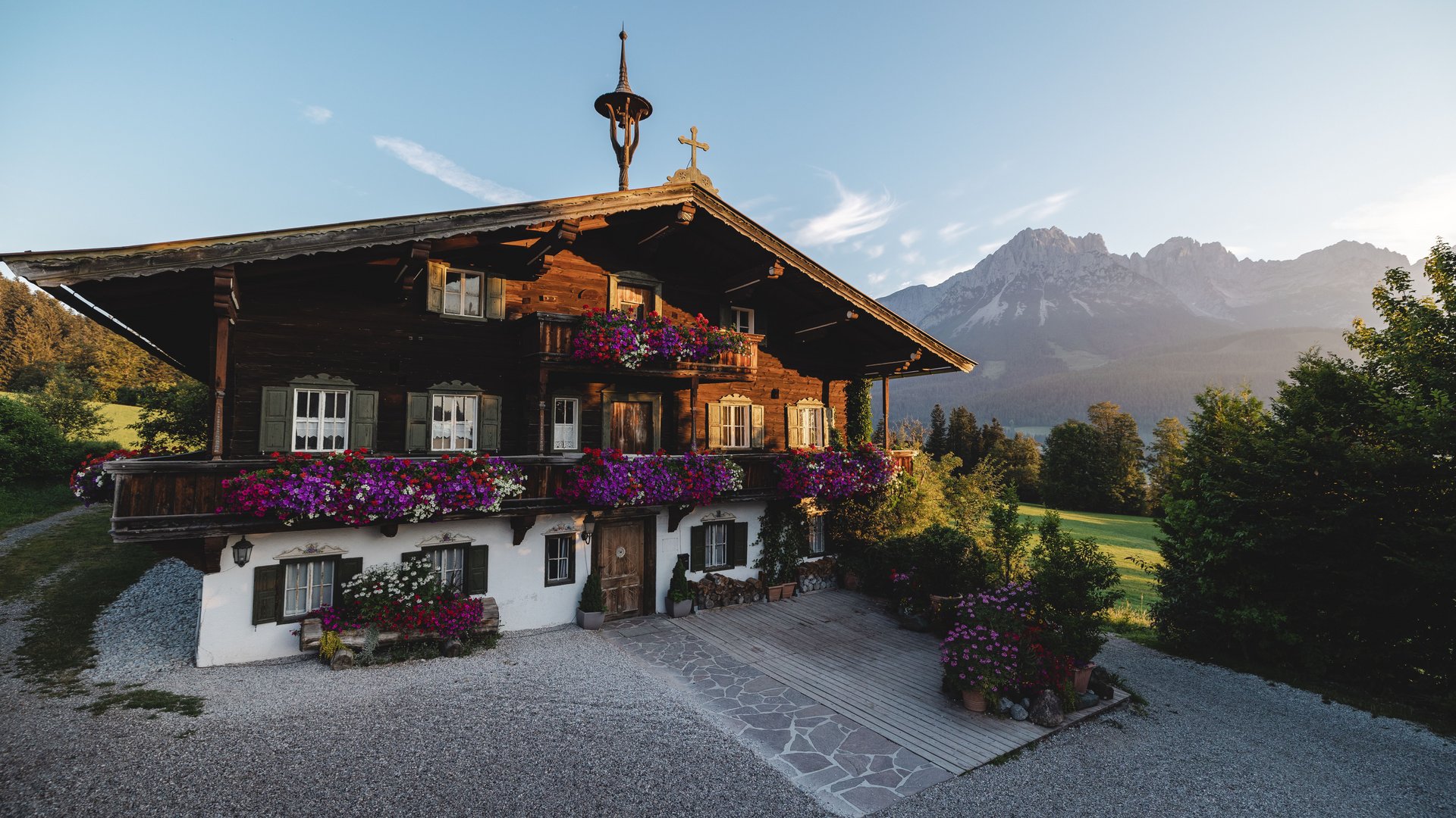 Traditionelles Holzhaus mit bunten Blumen und Alpen im Hintergrund bei Sonnenuntergang