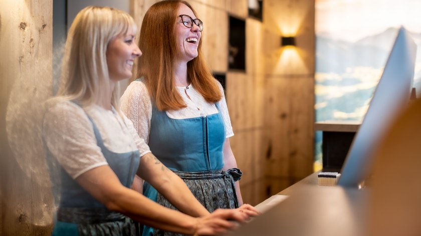 Welcome to our new website. Take a look around! Two women in traditional dresses smiling at a reception with wooden interior