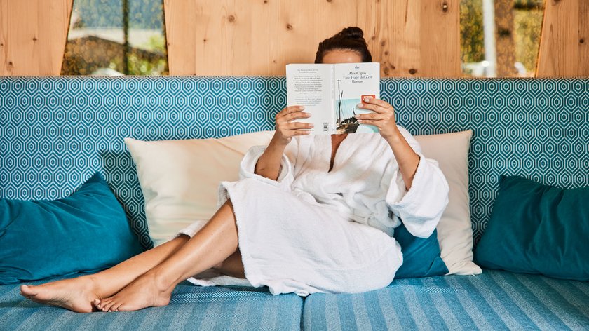 Die Körperbürstenmassage Person in Bademantel liest Buch auf blauem Sofa mit Kissen