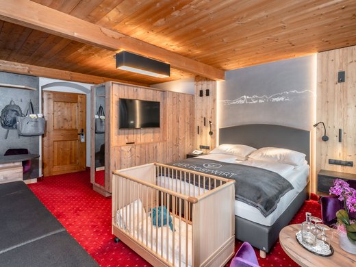 Family equipment at our family-friendly hotel in Soll. Cozy hotel room with baby crib, double bed, and wooden furniture