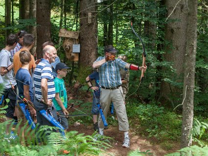 Söll: Ausflugsziele in der Umgebung Gruppe beim Bogenschießen im Wald mit einem Mann im Fokus beim Zielen
