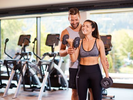 Fitnessstudio mit Hanteln Woman lifting dumbbells in gym with trainer assistance