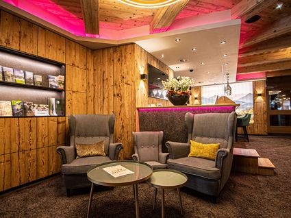 Kurzurlaub am Wilden Kaiser: Auszeit im Hotel Postwirt in Söll Gemütliche Hotel-Lounge mit grauen Sesseln, Holzwänden und pinker Deckenbeleuchtung