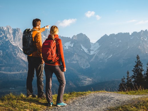 Sie suchen ein Hotel mit Fitnessstudio in Österreich? Zwei Wanderer mit Rucksäcken blicken auf bewaldete Berge mit Schnee