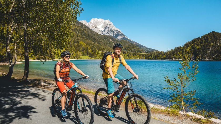 Die besten E-Bike Touren für Einsteiger und Profis Zwei Personen radeln an einem Seeufer mit Bergen im Hintergrund
