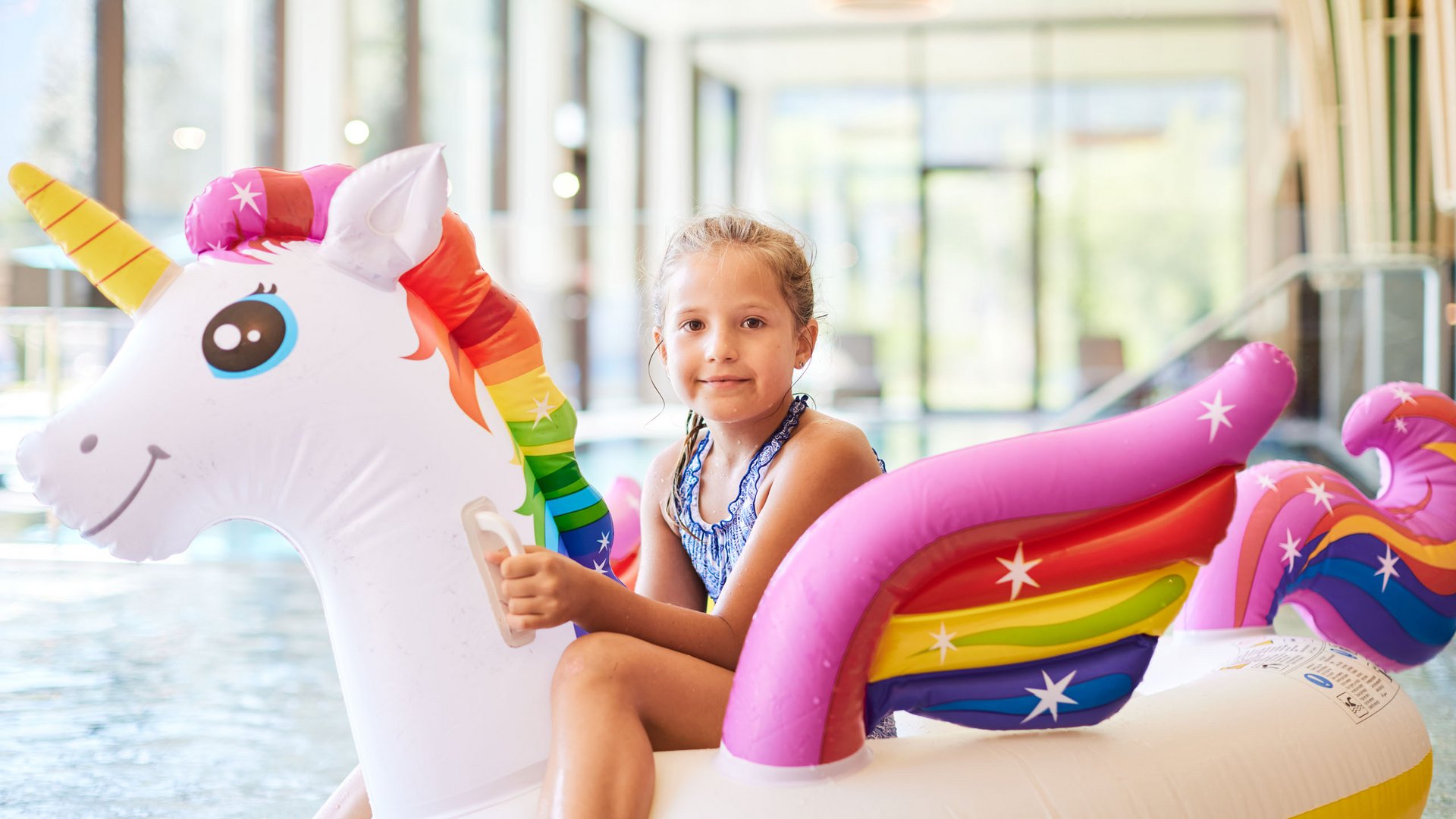 Mädchen auf aufblasbarem Einhorn im Hallenbad
