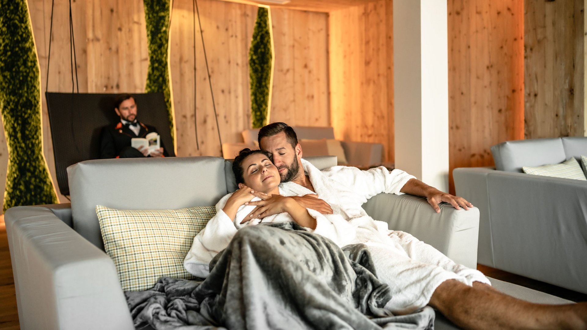 Paar in Bademänteln entspannt auf Sofa in gemütlichem Spa mit Holzinterieur