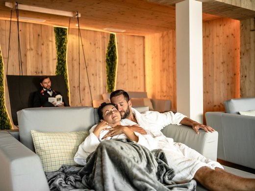 Holidays at the Postwirt: more than just in “a” hotel in Soll. Couple in bathrobes relaxing on sofa in cozy spa room with wooden walls
