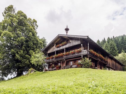Discover the benefits of the Wilder Kaiser GästeCard to be used in your holiday area- Old wooden house with flower garlands on a green hill
