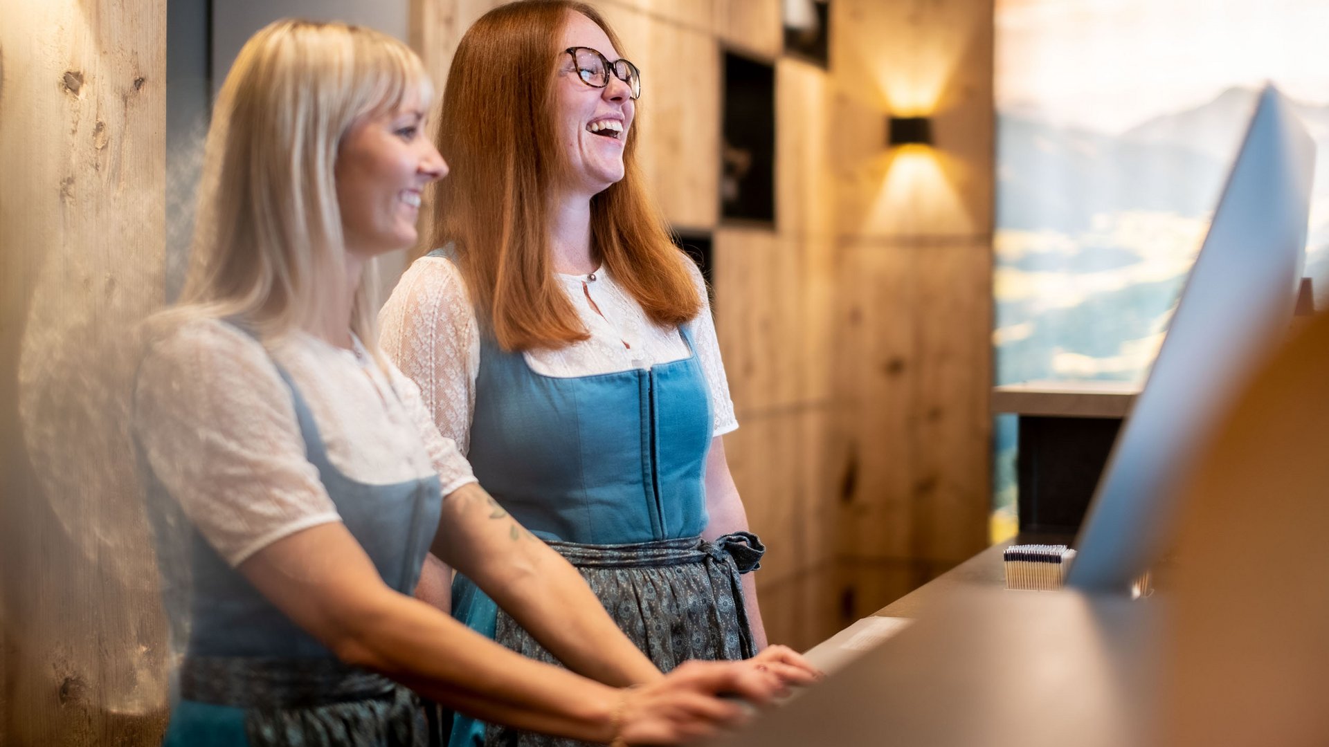 Holidays at the Postwirt: more than just in “a” hotel in Soll. Two women in traditional dresses laughing at a hotel reception desk