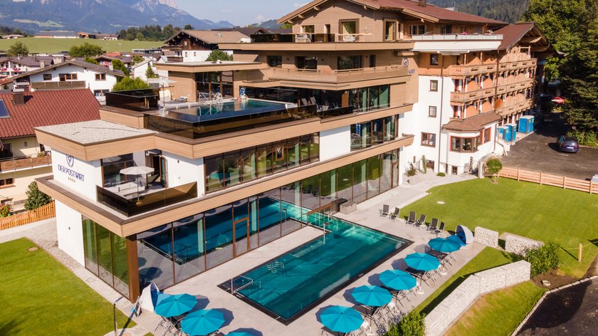 Urlaub ohne Hindernisse Moderner Wellnessbereich mit Pool und blauen Sonnenschirmen an einem Hotel in den Bergen