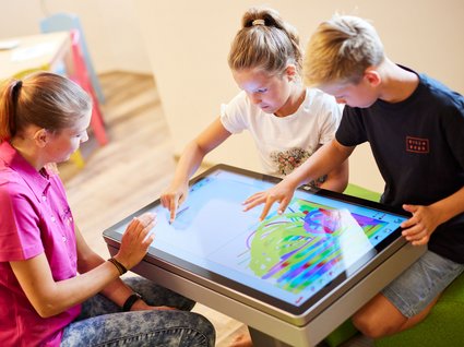 Fun and games in our family-friendly hotel in Soll Two kids and an adult using a large touchscreen table for drawing