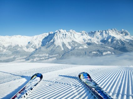 Discover the benefits of the Wilder Kaiser GästeCard to be used in your holiday area- Skis on freshly groomed slope with snow-covered mountains in the background