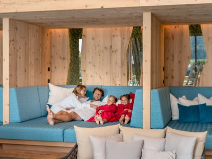Holidays at the Postwirt: more than just in “a” hotel in Soll. Family relaxing in bathrobes on blue sofa in a modern wooden room