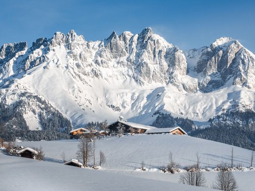 Postwirt Söll: Ihr Langlaufhotel in Tirol Schneebedeckte Berghütte vor beeindruckenden, schneebedeckten Gipfeln bei klarem Himmel