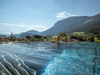 Der Postwirt: Hotel mit Infinitypool in Tirol Paar entspannt im Infinity-Pool mit Bergblick bei sonnigem Wetter