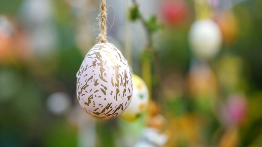Ostertraditionen in Tirol: Feste und Bräuche Dekoratives Osterei mit goldenen Mustern an Schnur aufgehängt vor unscharfem Hintergrund