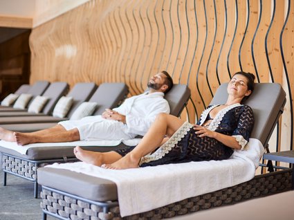 Der Postwirt: Hotel mit Infinitypool in Tirol Paar entspannt sich auf Liegestühlen in einem modernen Spa mit Holzwand