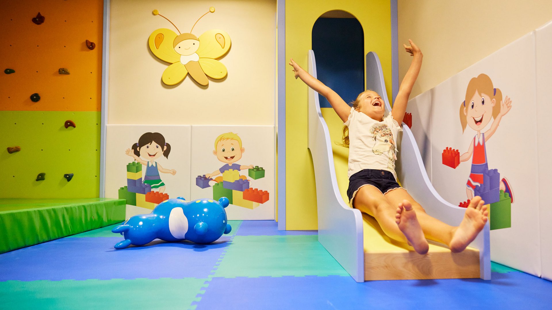 Fun and games in our family-friendly hotel in Soll Happy girl sliding in colorful indoor play area with wall art and toys