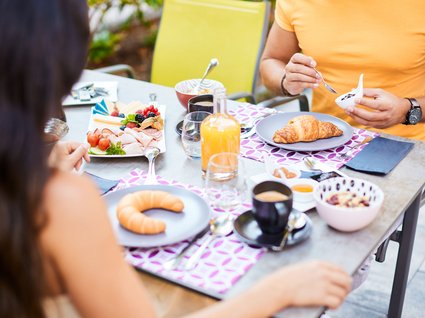 Holidays at the Postwirt: more than just in “a” hotel in Soll. Two people having breakfast outdoors with croissants, cold cuts, coffee, and orange juice
