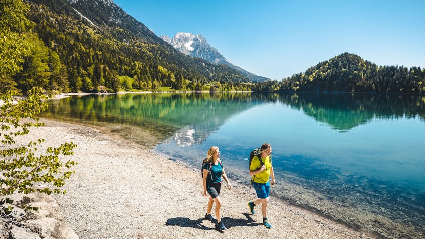Rundweg um den Hintersteiner See Paar wandert am Ufer eines alpinen Sees mit Bergen und blauem Himmel im Hintergrund
