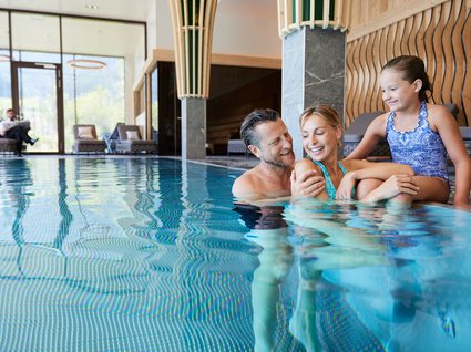 Familie im Innenpool des Hotels Eine lächelnde Familie genießt gemeinsam das warme Wasser im Innenpool eines Hotels, umgeben von modernem Design und großen Fenstern.