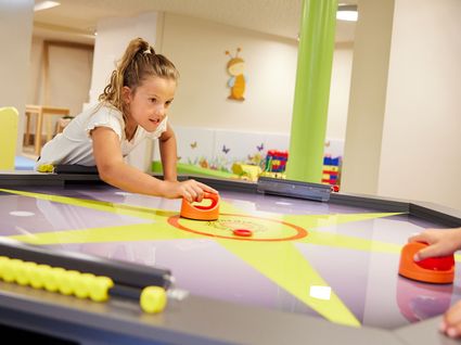Kurzurlaub am Wilden Kaiser: Auszeit im Hotel Postwirt in Söll Mädchen spielt Airhockey in einem Spielzimmer mit bunten Wänden
