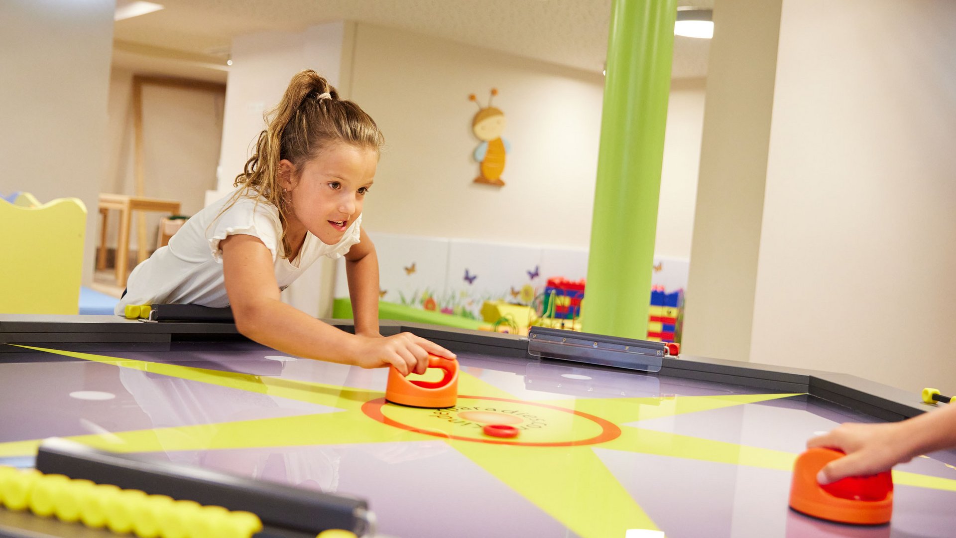 Fun and games in our family-friendly hotel in Soll Girl playing air hockey in a colorful playroom