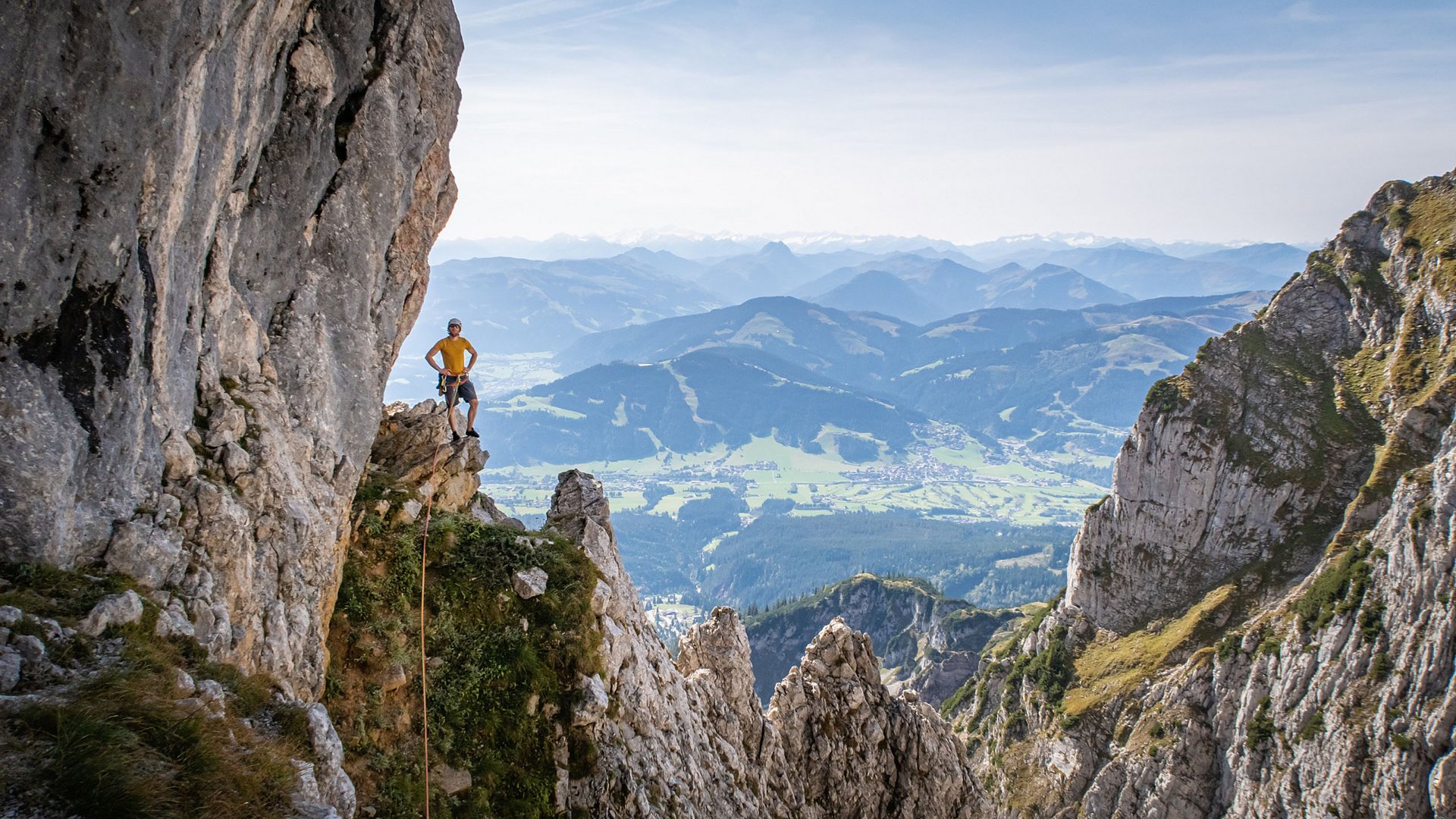 Discover the benefits of the Wilder Kaiser GästeCard to be used in your holiday area- Climber on rock ledge with panoramic view of mountains and valley