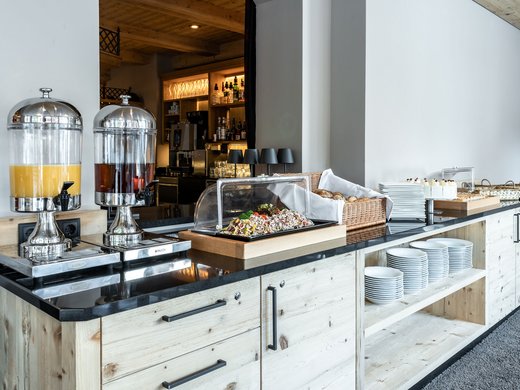 Hotel in Söll: the Postwirt Buffet with drink dispensers, salad, rolls, and cakes on wooden counter