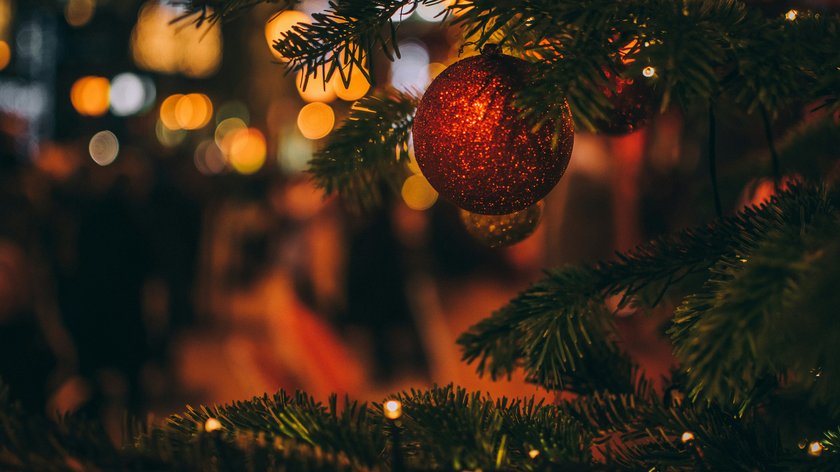 Traditionen und Bräuche zur Weihnachtszeit in Tirol Roter Weihnachtsbaumschmuck an Tannenzweig mit verschwommenem Lichterhintergrund